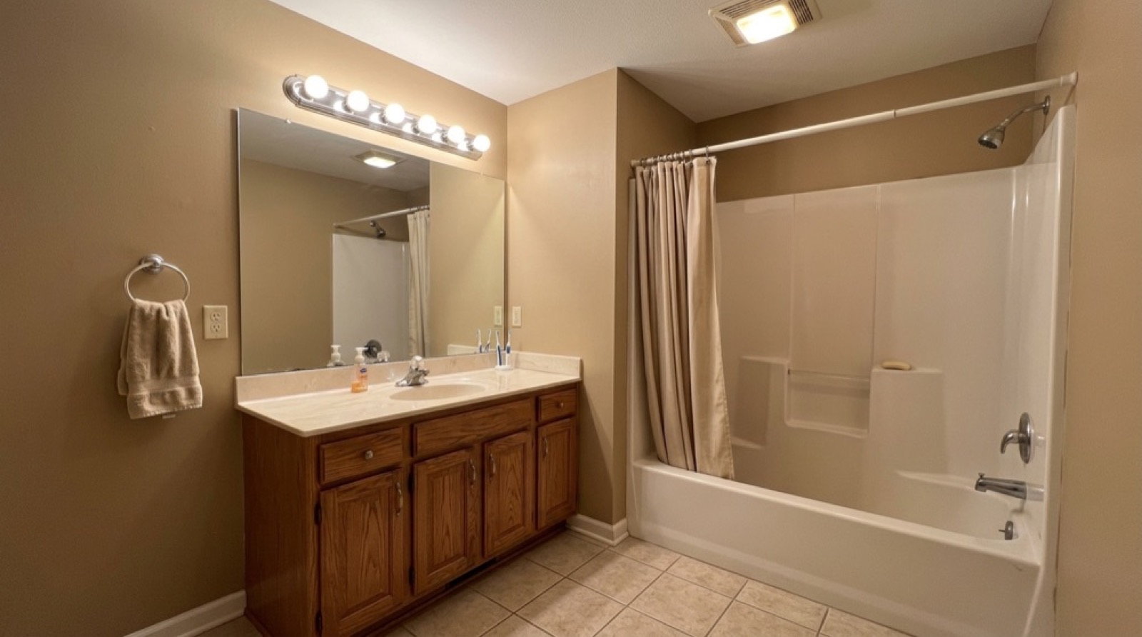 Before: the same bathroom with a dated oak vanity and a tub with a shower curtain