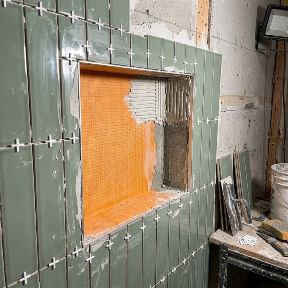Shower niche mid-tile, with orange waterproofing membrane visible before the final tiles go on